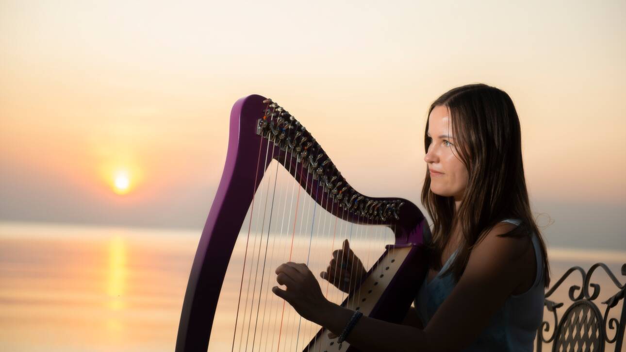 Beautiful girl in a flower dress plays on a Celtic harp by the sea at sunset